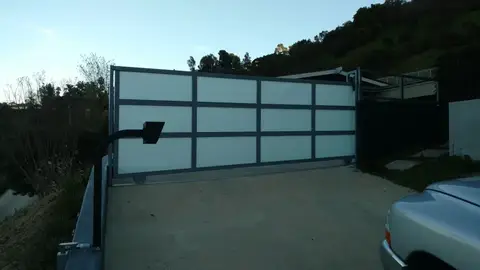 Modern sliding driveway gate with frosted panels at a hillside home