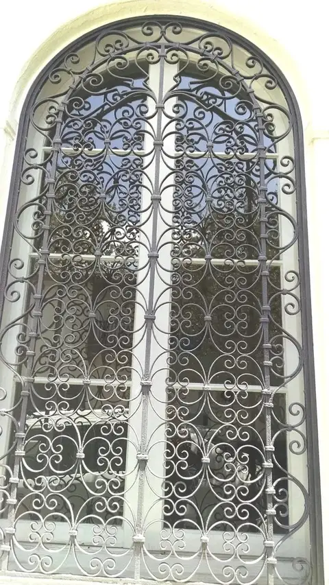 Arched iron window grille with fine scrollwork over French doors