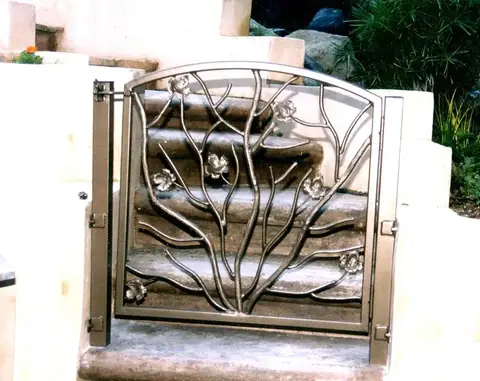Pedestrian gate with a hand-forged tree branch design on stone steps