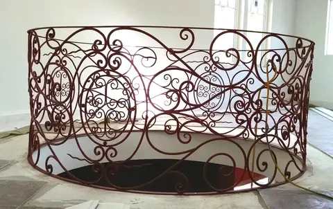 Circular stair-opening railing in a bronze finish, wrapped in hand-forged scrollwork