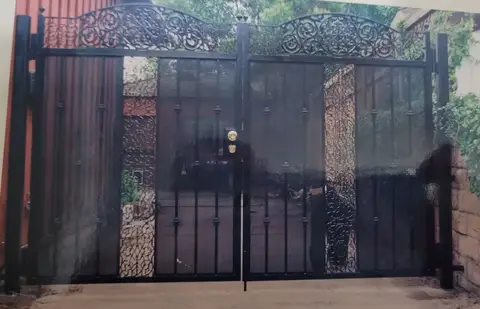 Black double driveway gates with a scrollwork header and privacy panels