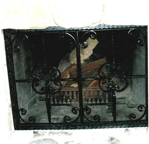 Black fireplace screen with rosette medallions in a stone fireplace