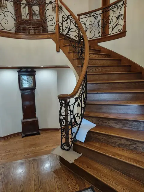 Curved wooden staircase with a scrollwork iron railing and wood handrail