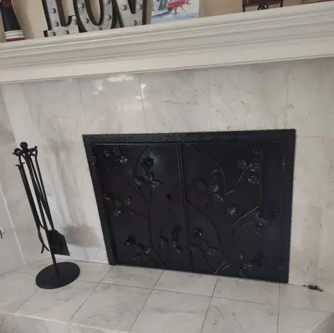 Black fireplace doors with a vine design in a marble fireplace