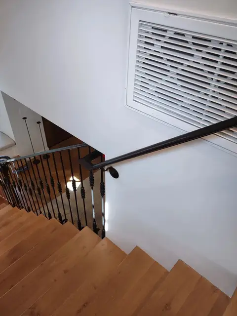 Stair railing with slim black balusters on wood stairs, viewed from the top