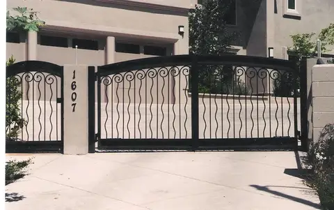 Driveway gates with wavy vertical bars and a matching pedestrian gate