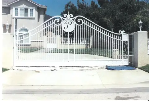 White estate driveway gate with a custom monogram medallion