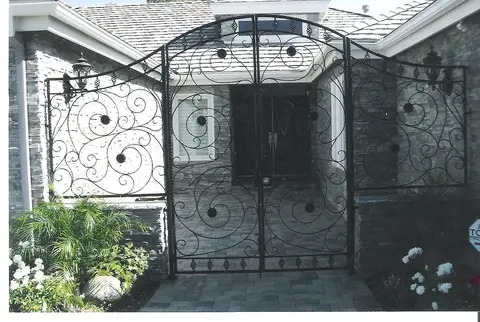 Tall double courtyard gates with full scrollwork at a stone home entry