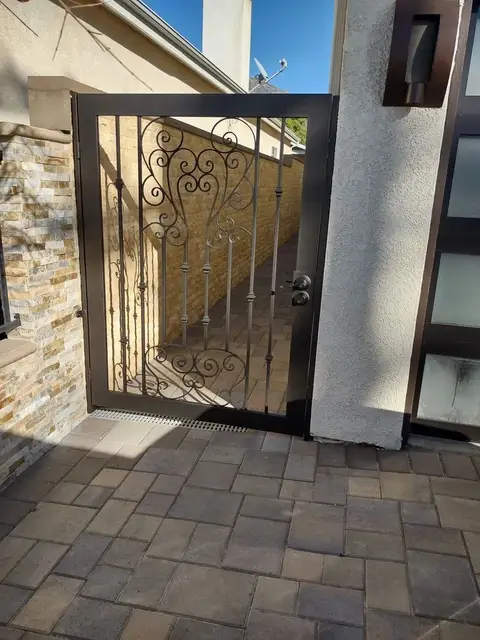 Pedestrian gate with scrollwork at a paver courtyard entry