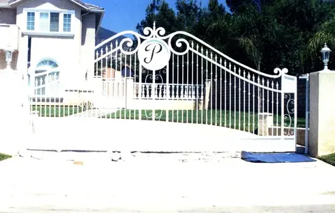 White driveway gate with a custom monogram medallion at an estate entry