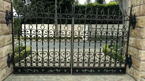 Double driveway gates with spear finials and heart scrollwork between stone pillars