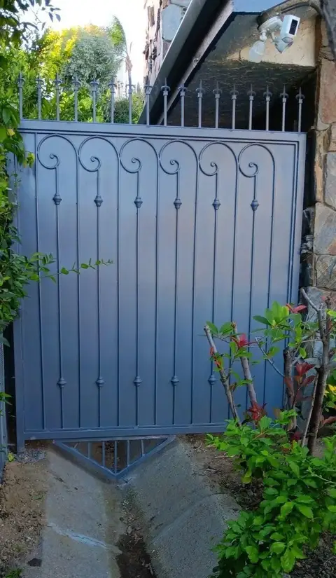 Blue-gray pedestrian gate with vertical bars and scroll details